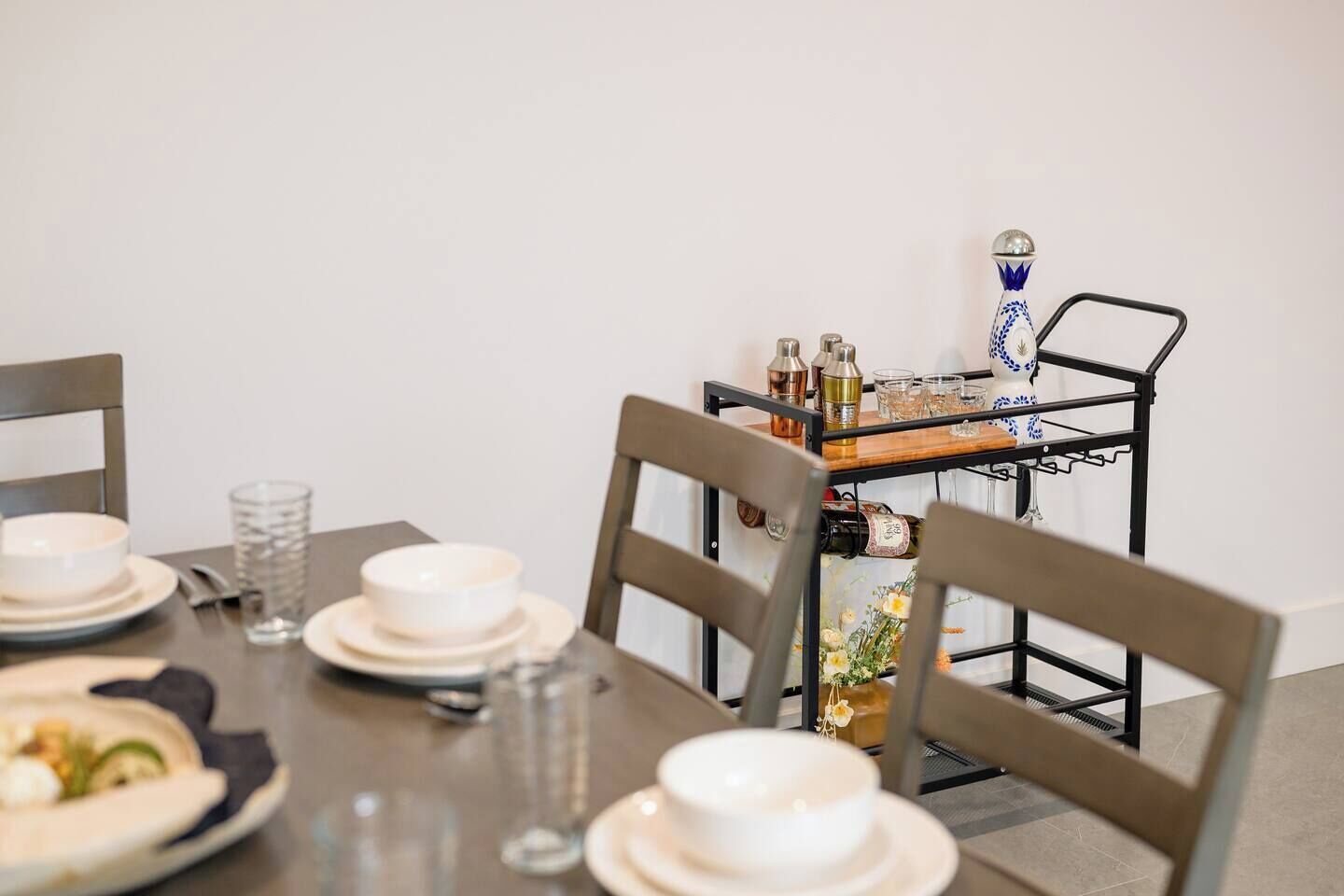 Ett matbord med tallrikar, glas och ett metallställ med flaskor och en dekorativ vas.
