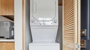 Une petite buanderie comprenant un lave-linge et un sèche-linge, des armoires en bois et une porte à persiennes.