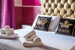 Un lit bien fait, avec deux oreillers, l’un portant l’inscription « KING » et l’autre « QUEEN », et un ensemble de serviettes posé à côté.