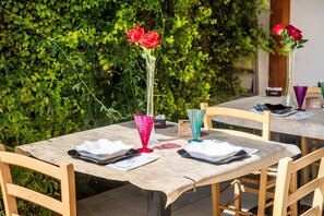 Un espace de restauration en plein air avec des tables disposées pour deux personnes, chacune agrémentée d’un vase de fleurs et d’un set de table.