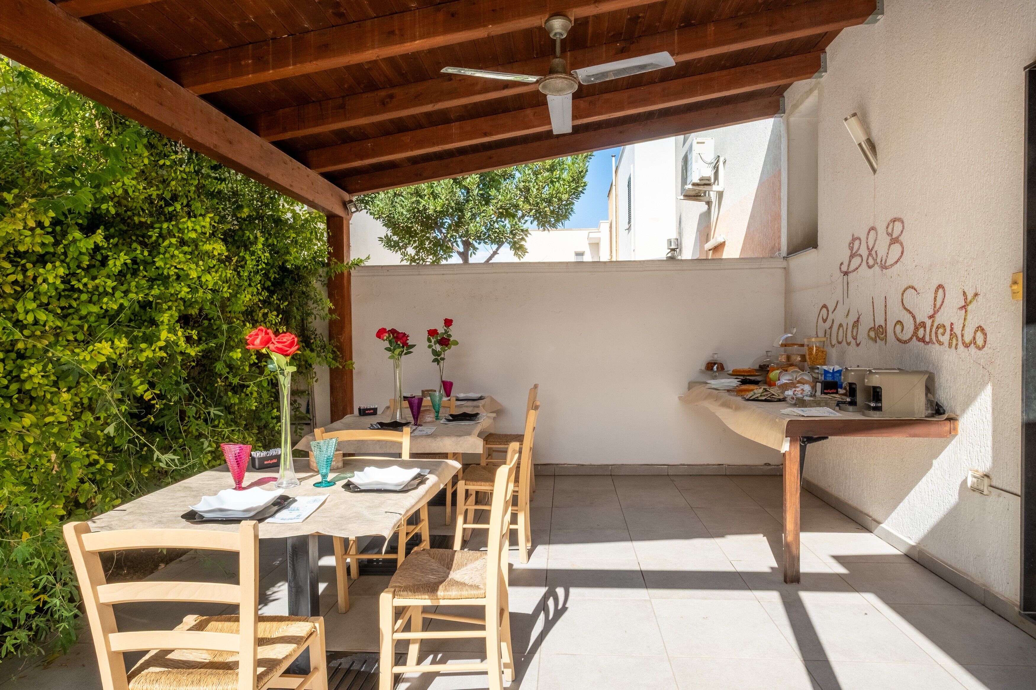 Une terrasse extérieure avec des tables et des chaises en bois, un ventilateur de plafond et un mur couvert de graffitis.