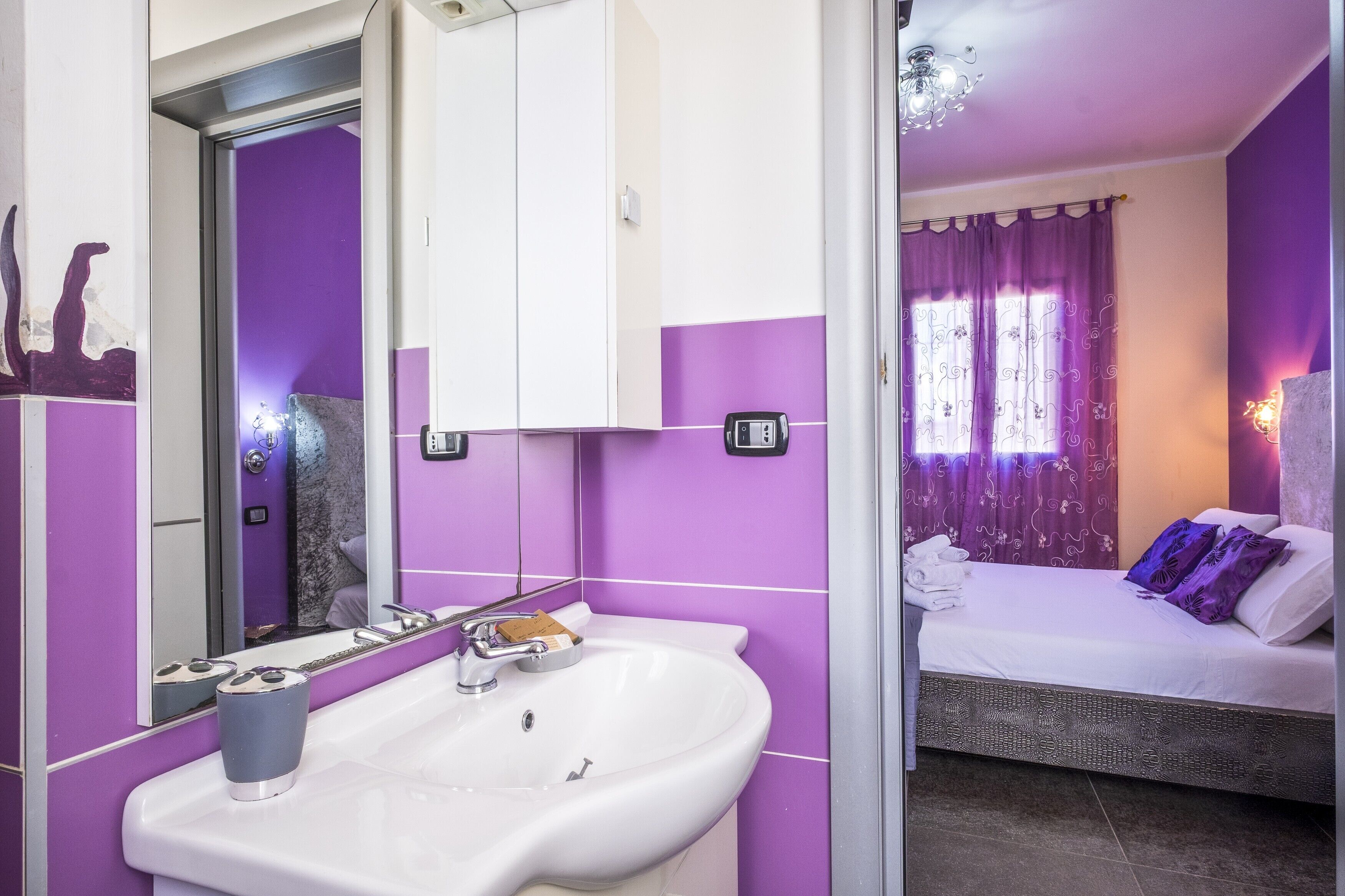 A bathroom with a sink, mirror, and a bed with a window.