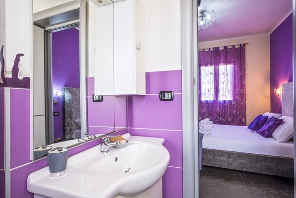 A bathroom with a sink, mirror, and a bed with a window.