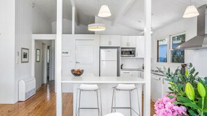 A modern kitchen with white cabinetry, a central island with bar stools, a refrigerator, and a microwave.