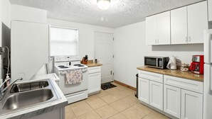 A kitchen with white cabinets, a stove, a microwave, and a coffee maker. - Charming 1-bedroom condo in cool Crystal River with AC (Crystal River)