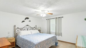 A bedroom with a bed, a nightstand, a ceiling fan, a window with curtains, and a wall-mounted shelf with decorative items. - Charming 1-bedroom condo in cool Crystal River with AC (Crystal River)