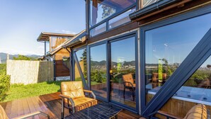 Una terraza moderna al aire libre con paredes de vidrio, mobiliario de madera y vistas al paisaje.