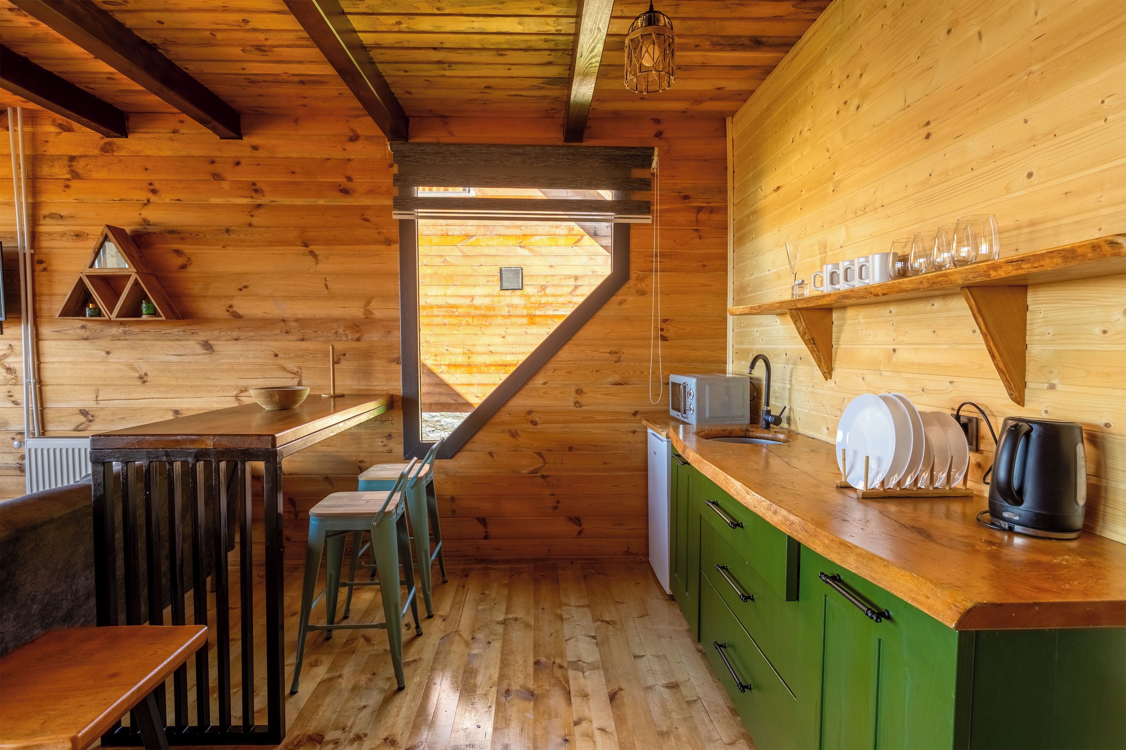 Un intérieur en bois comprenant un espace cuisine avec un comptoir, des armoires vertes et un coin repas avec un banc et des chaises.