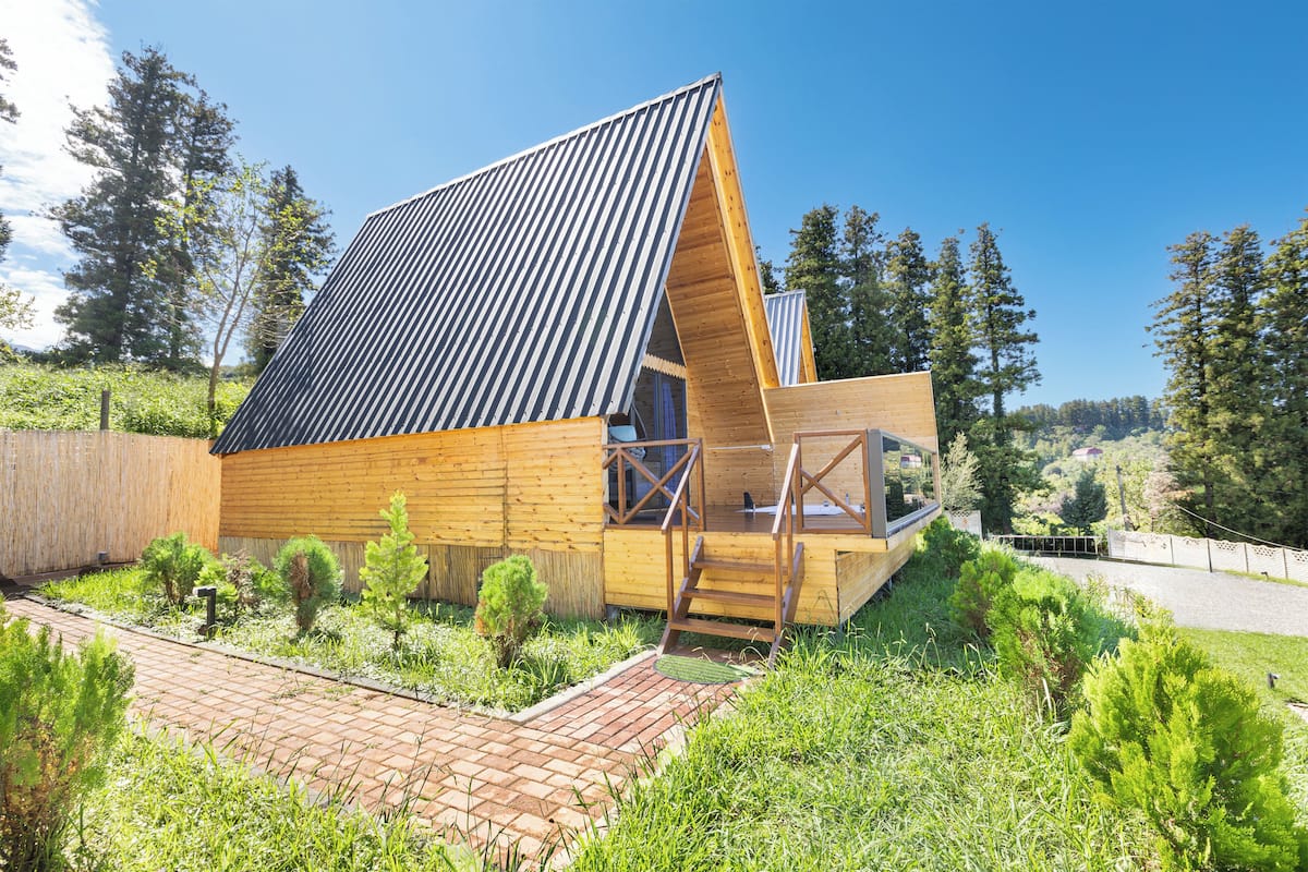 A modern wooden cabin with a sloped roof, a wooden deck, and a small staircase leading to a balcony.