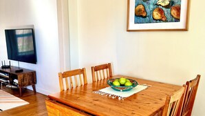 A dining area with a wooden table, six chairs, and a bowl of green apples on a placemat. - Cozy  Coastal by Beaches & Redwoods (McKinleyville)