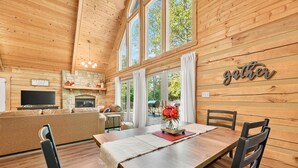A wooden interior with a dining table, chairs, a TV, and a fireplace. - Log Cabin Luxury Near IU & Lake Monroe (Bloomington)