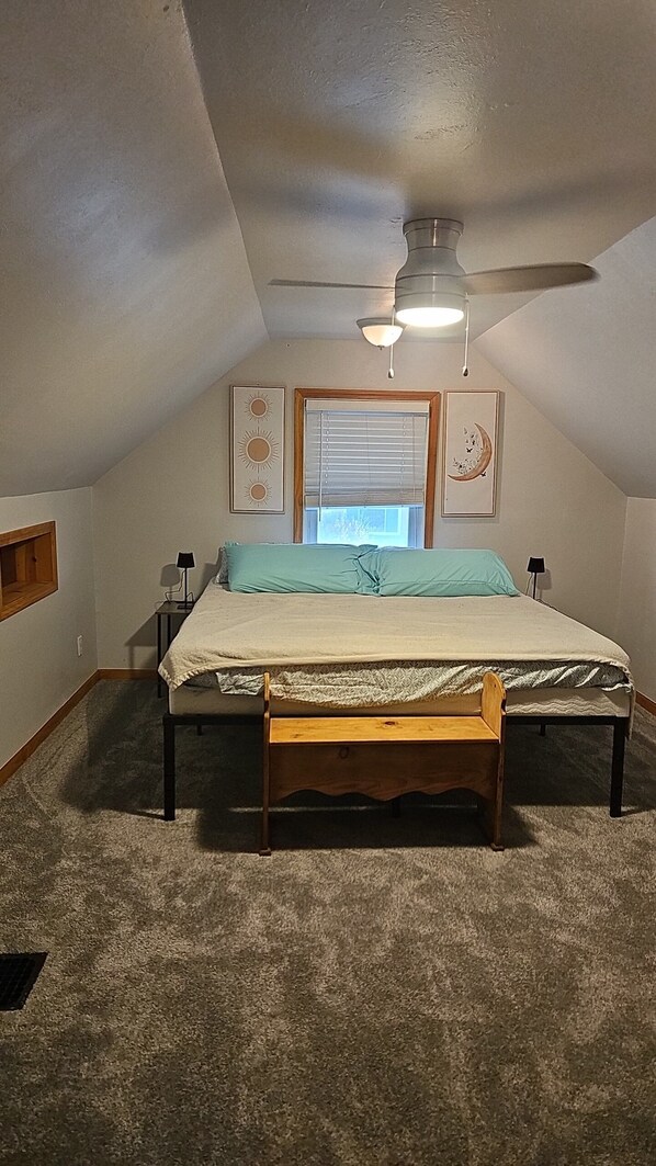 A bedroom with a bed, a ceiling fan, a window with blinds, and two wall-mounted lamps.