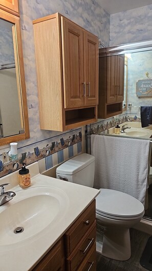A bathroom with a white sink, wooden cabinets, a toilet, and a shower curtain.