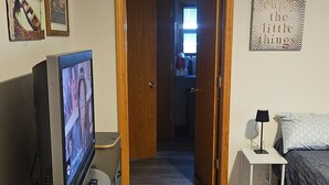 A room with a television on a dresser, a bed with a patterned blanket, a small white nightstand with a lamp, and a door leading to a hallway. - Spacious Family Retreat w/ADA Ramp & ADA bathroom (Maumee)
