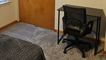 Een slaapkamer met een bed, een bureau met stoel, een houten deur en een schilderij aan de muur.