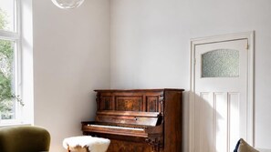Un pianoforte in una stanza con una finestra, una porta con pannello decorativo e una sedia.