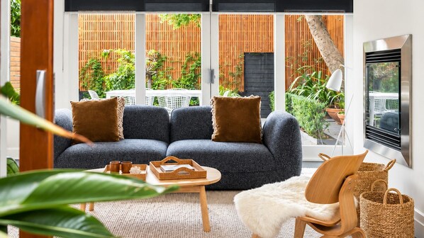 A modern living room with a sectional sofa, a wooden coffee table, a white furry rug, and a view of a garden through large windows.