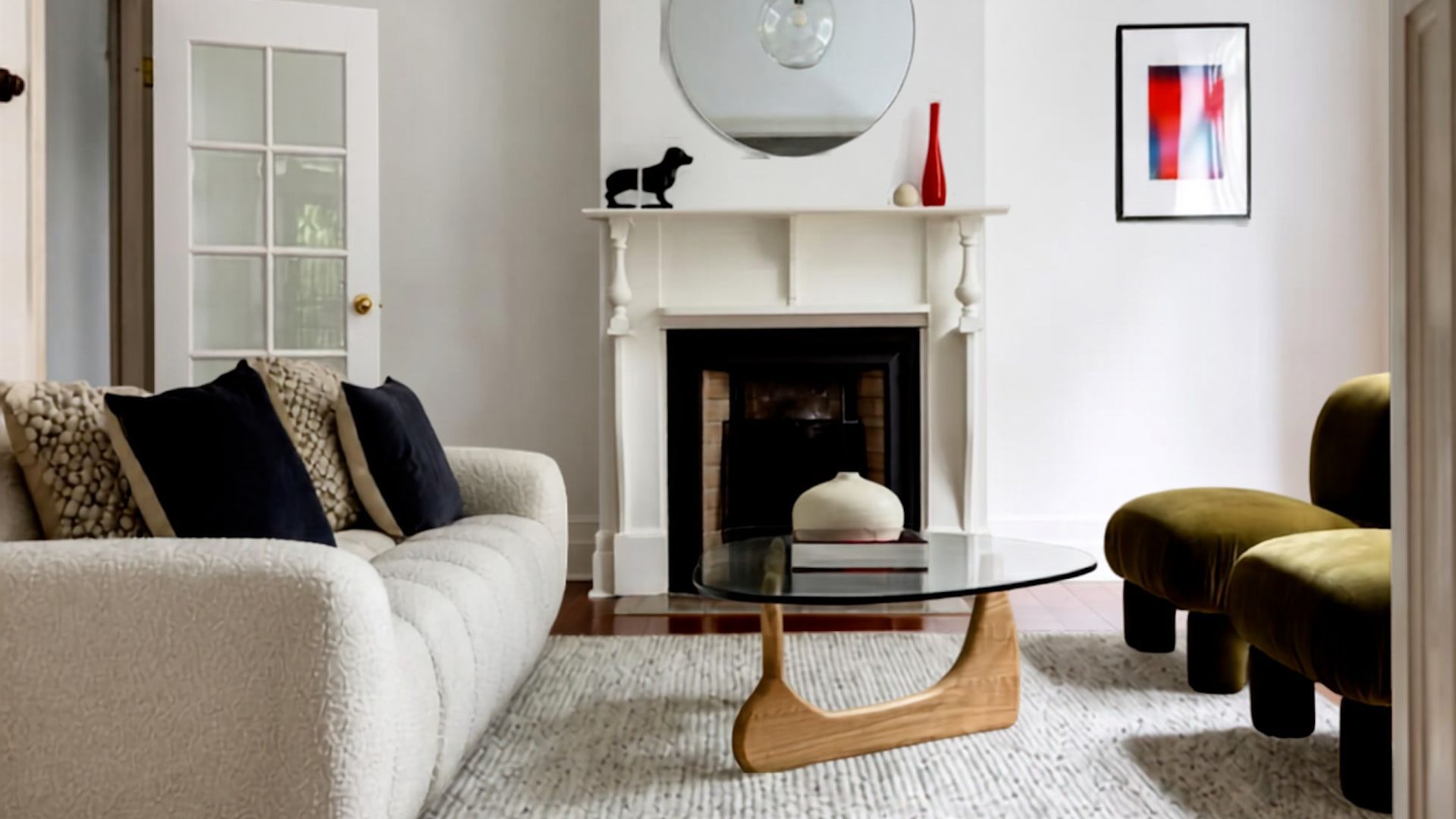 A living room with a white sofa, a glass coffee table, a fireplace, and a framed abstract painting.