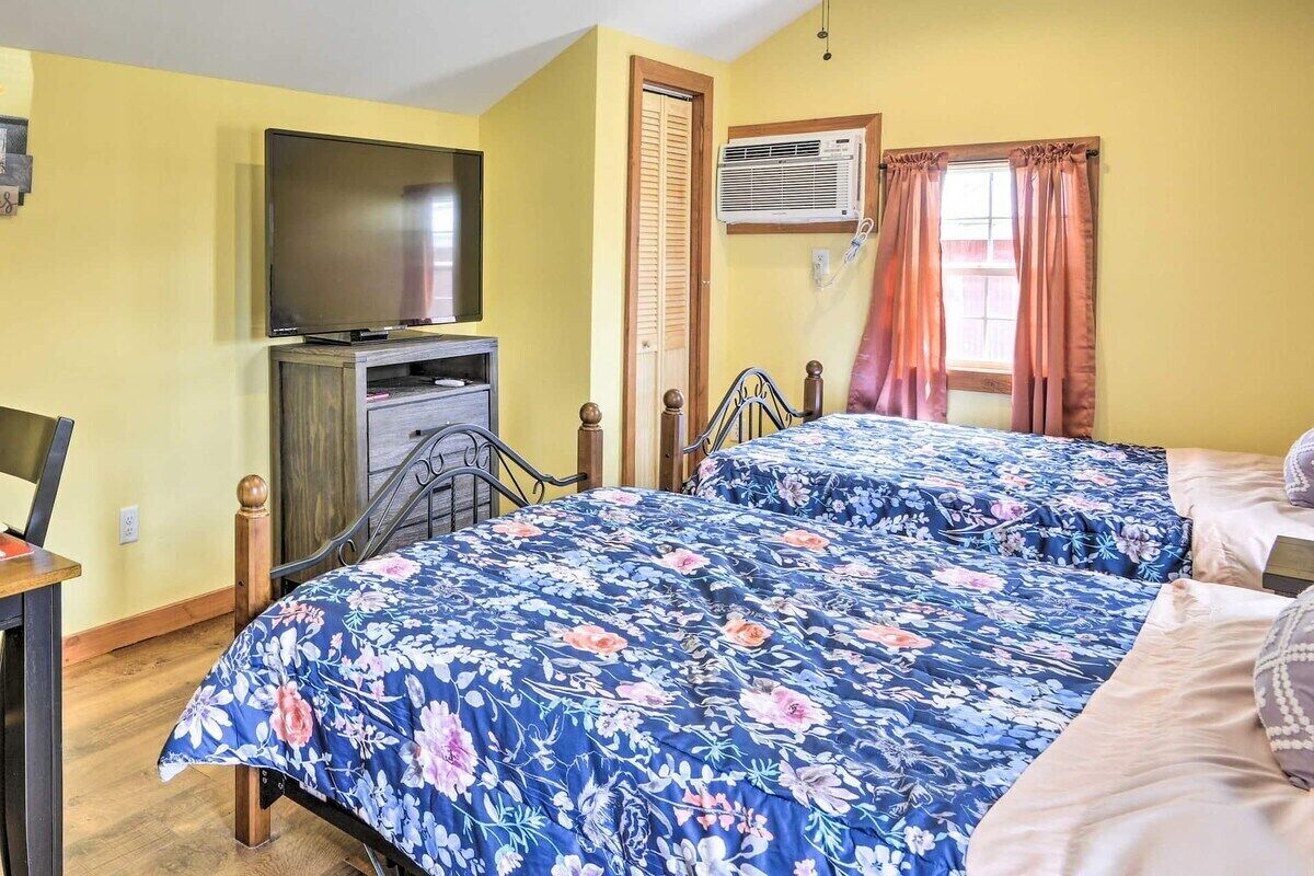 A room with two beds, a television, an air conditioning unit, and a window with curtains.
