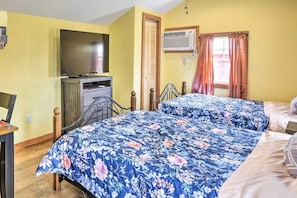 A room with two beds, a television, an air conditioning unit, and a window with curtains.