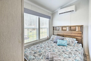 Een slaapkamer met een bed, een raam met jaloezieën, een airconditioning en een bed met een decoratieve spreideken.