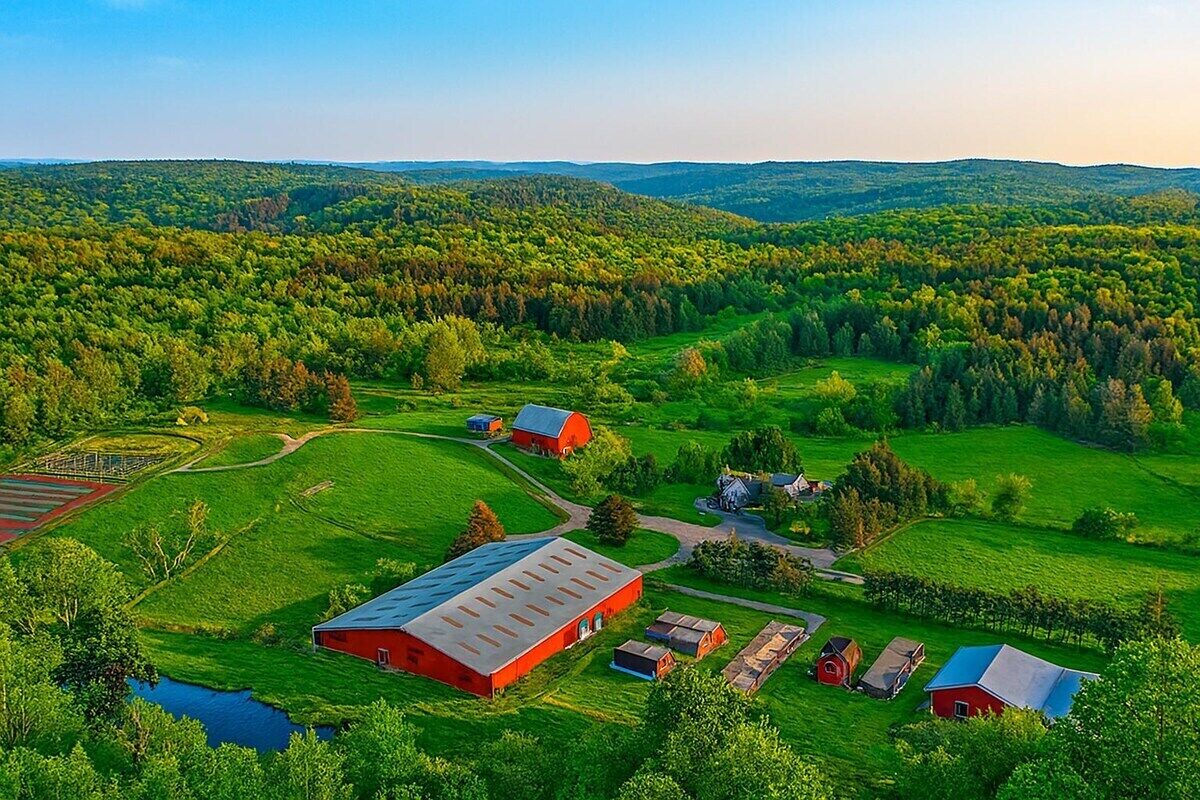 A rural landscape with a large red barn, smaller red buildings, and a winding road.