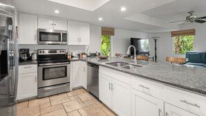 A modern kitchen with white cabinets, stainless steel appliances, a granite countertop, and a ceiling fan. - Kaanapali Plantation By Chase N Rainbows (Lahaina)