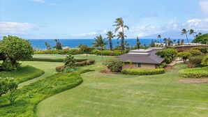 A golf course with a house in the foreground, surrounded by lush greenery and palm trees, with a view of the ocean and a mountain in the background. - Kaanapali Plantation By Chase N Rainbows (Lahaina)