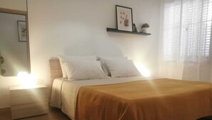 Een slaapkamer met een bed, nachtkastje en een wandplank met een lijst en een kleine plant.