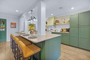 A modern kitchen with a central island, bar stools, green cabinets, and pendant lighting.