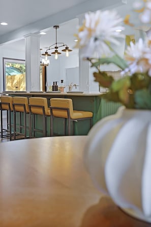 A modern kitchen with a bar area, featuring a wooden countertop, bar stools, and a vase with flowers.