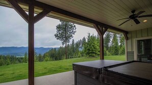 Ein überdachter Außenbereich mit Whirlpool, Holzbalken und Blick auf eine grüne Landschaft und Berge.