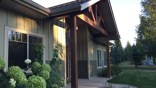 Ein modernes Haus mit überdachter Veranda, großen Fenstern und einem gepflegten Garten.