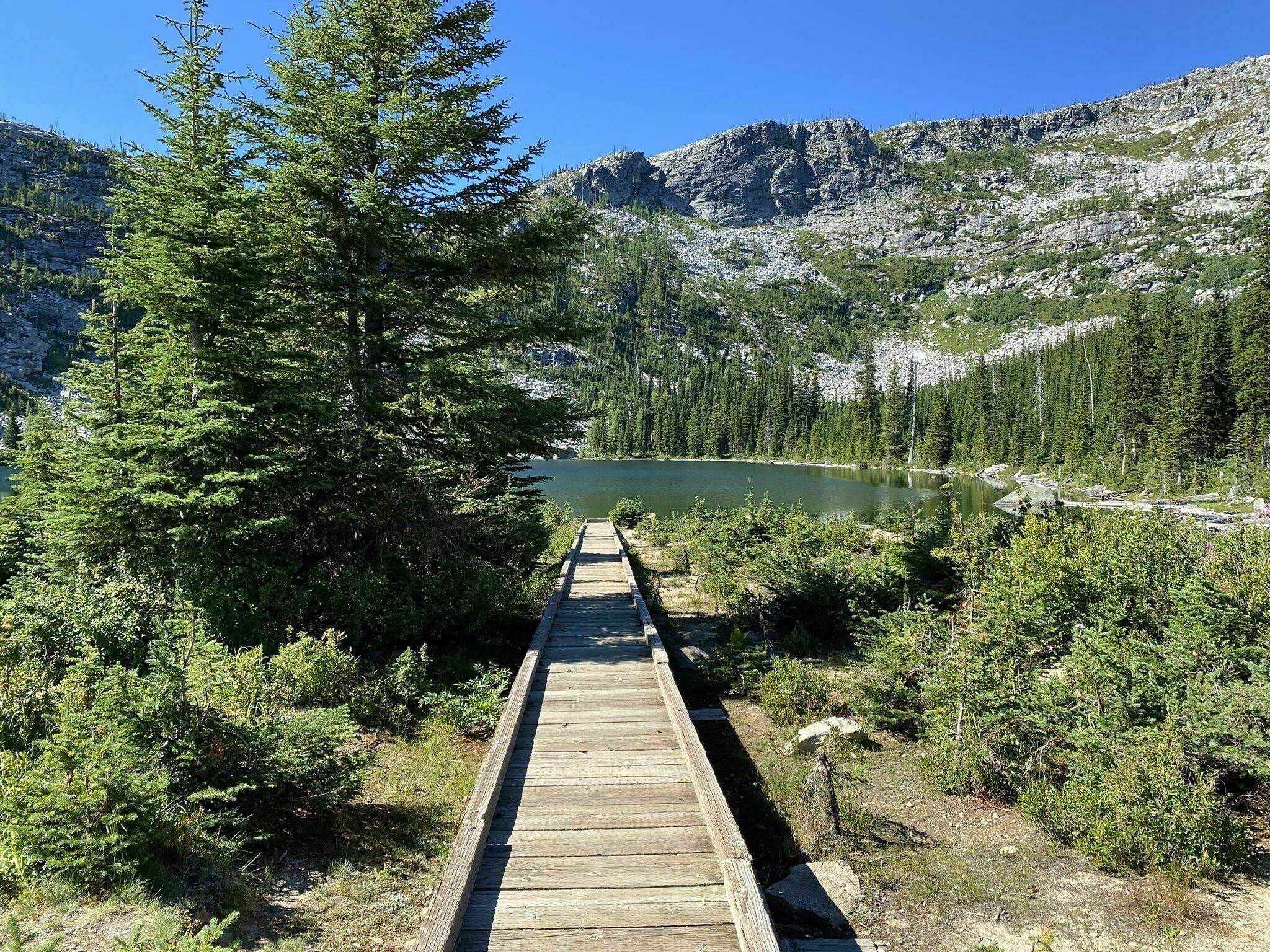 Une promenade en bois qui mène à un lac entouré d’une forêt dense et de montagnes rocheuses.