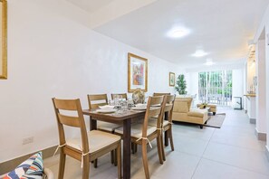 Ein Essbereich mit einem Holztisch, gedeckt für vier Personen, umgeben von Holzstühlen. Im Hintergrund befindet sich eine Couch und eine kleine Pflanze.