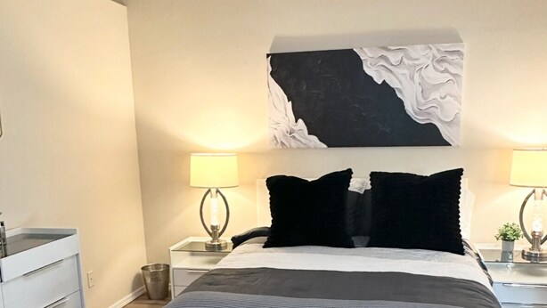 Un dormitori modern amb un llit gran, dues taules de nit, un calaix blanc i un quadre abstracte en blanc i negre penjat sobre el llit.