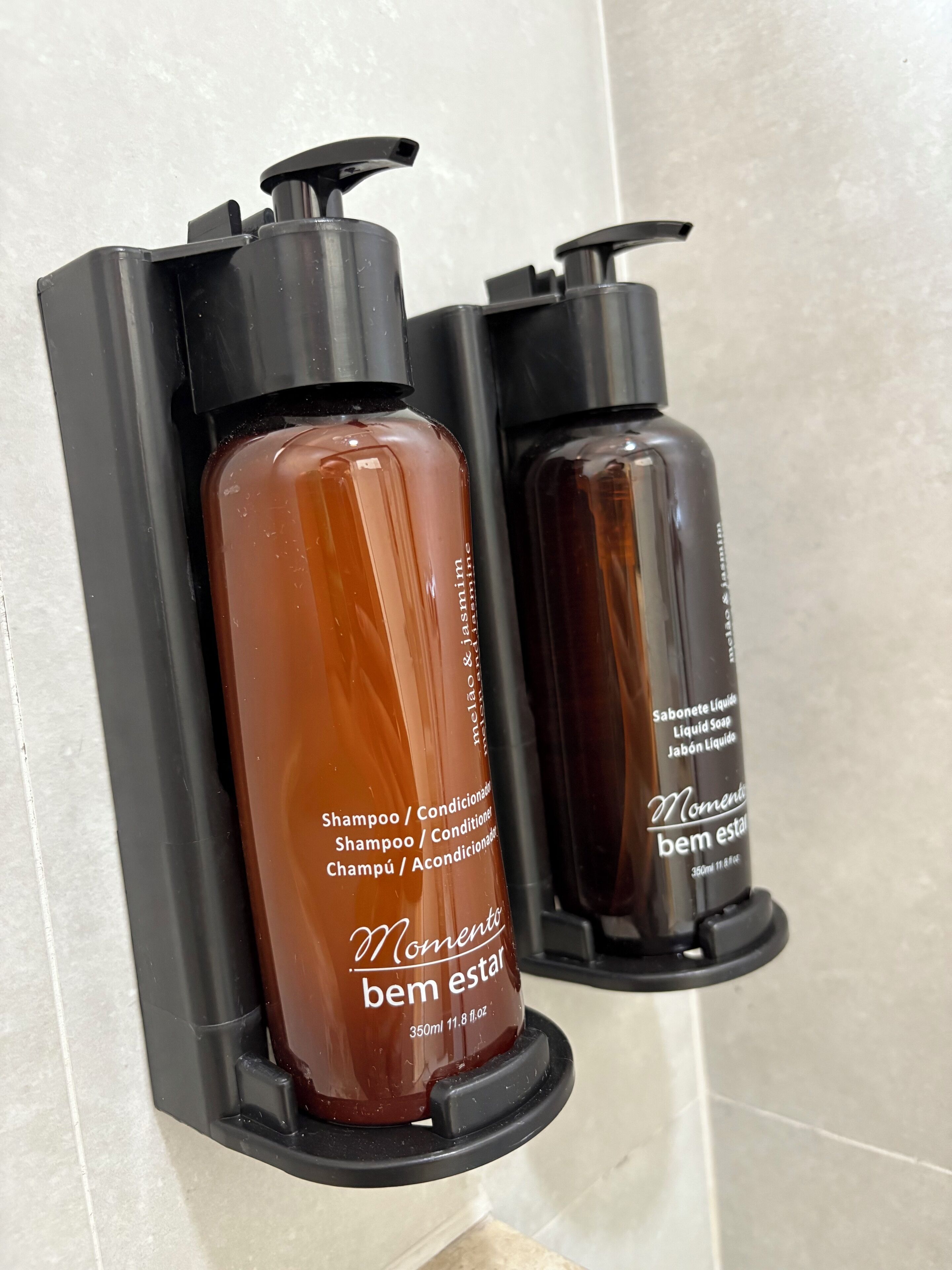 Two bottles of shampoo and conditioner in a black soap dispenser holder.