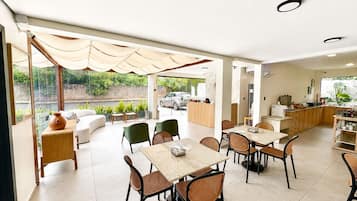 A modern dining area with multiple tables and chairs, a kitchen area with appliances, and a reception desk.