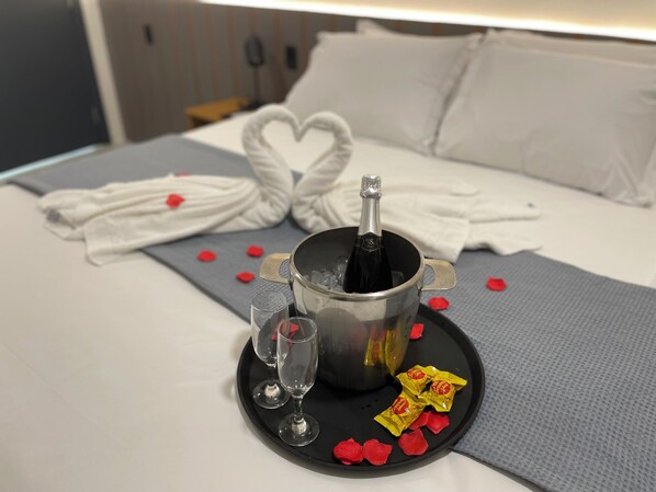 A bed with a heart-shaped towel, a bottle of champagne, two glasses, and rose petals on a tray. - Belaris COMFORT  (São Luís)