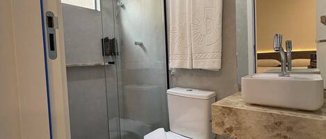 Un baño moderno con cabina de ducha de vidrio, inodoro y lavabo con espejo.