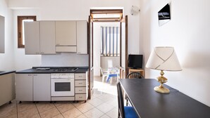 A compact kitchen with a stove, oven, and cabinets, a dining table with a lamp, and a view of the outside through a door. - Porto Cesareo apartment 300 meters from the sea (Porto Cesareo)