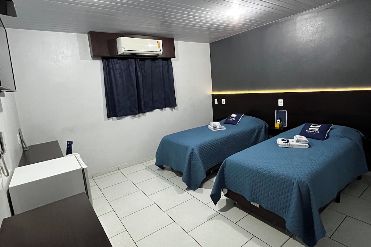 Une chambre d’hôtel avec deux lits, un bureau, un appareil de climatisation et une fenêtre avec des rideaux.