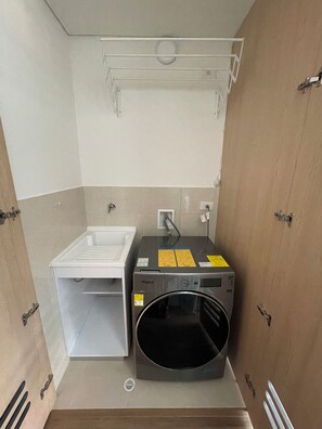 Une petite buanderie équipée d’un lave-linge et d’un sèche-linge Whirlpool, d’un évier blanc et d’un porte-serviettes.