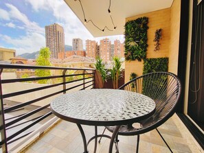 Een balkon met een ronde tafel en een stoel, een plant in pot en een groen wandpaneel.