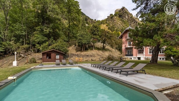 Piscina com espreguiçadeiras e uma pequena cabana de madeira, tudo envolto por árvores e uma encosta.