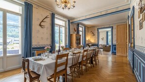 Uma sala de jantar com uma mesa comprida posta para refeição, com cadeiras de madeira de ambos os lados.