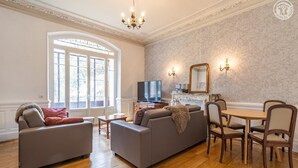 Uma sala de estar com sofá, televisão e área de jantar com cadeiras e mesa.