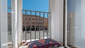 Un balcon agrémenté d’un coussin à motifs, une porte vitrée et une vue sur un immeuble doté de balcons.