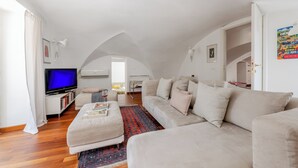 Un salon spacieux avec un grand canapé, un téléviseur et un tapis à motifs.