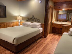 A neatly arranged bedroom with a wooden headboard, a bedside lamp, and a wooden floor.